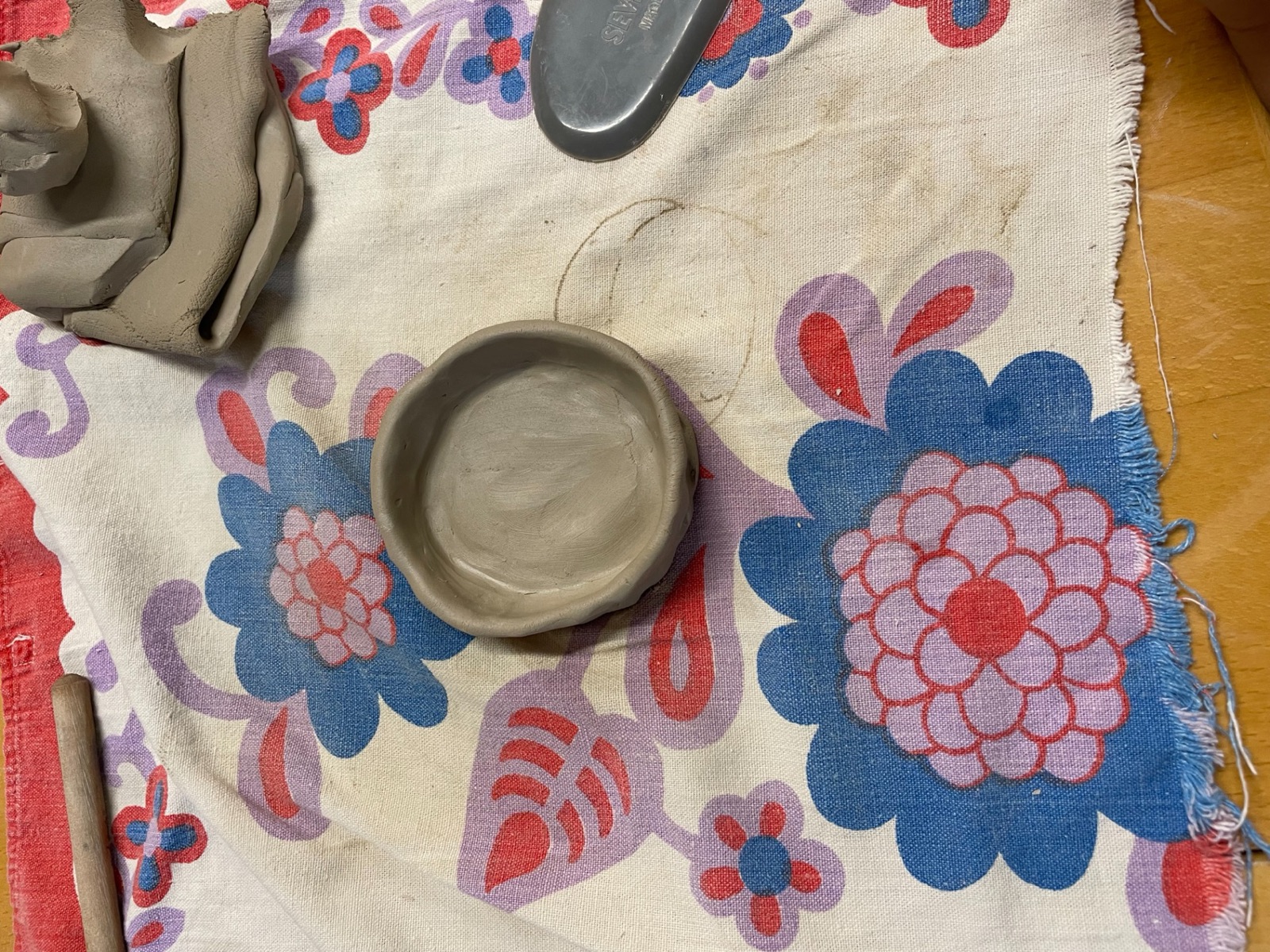 Håndformet pinch-skål i råt ler på blomstret dug